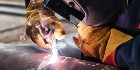 Saldatura tubi con guanti protettivi e maschera. Scintille e fumo illuminano il metallo.
