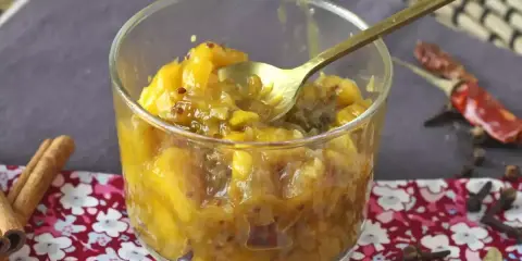 En skål med gyllene mango chutney, perfekt för ditt mango chutney recept. Kryddor som kanel och chili ligger bredvid.