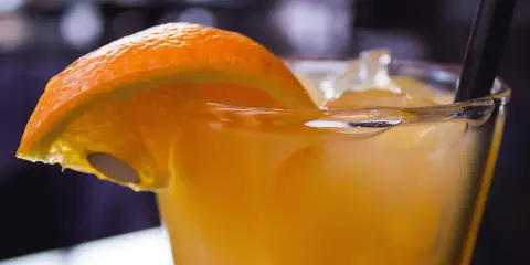 Orzeźwiający drink z suchym lodem, ozdobiony plasterkiem pomarańczy. Dymiący napój wygląda magicznie.