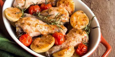 Delizioso pollo al forno con patate e pomodorini, guarnito con rosmarino fresco. Un piatto invitante e saporito.