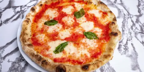 Pyszna pizza napoletana z pomidorami, mozzarellą i bazylią na białym talerzu, na tle marmurowego wzoru.