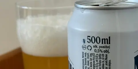 Piwo z puszki z etykietą "alk. poniżej 0,5% obj." obok szklanki z pianką. Sprawdzamy, ile promili ma to piwo.