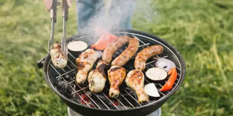 Rozpalanie grilla to sztuka! Na ruszcie skwierczą kiełbaski, kurczak i warzywa. Dym unosi się, zapowiadając pyszny posiłek.