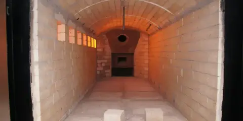 Wnętrze krematorium, gdzie czeka całun do kremacji. Pomieszczenie wyłożone cegłami, z łukowym sklepieniem i widocznym otworem pieca.