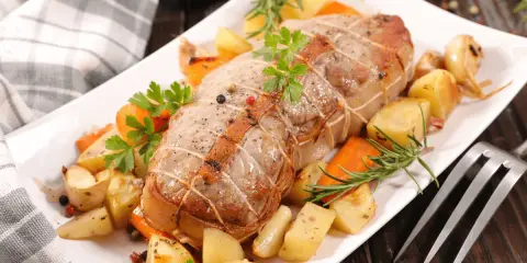 Rôti de veau savoureux, entouré de pommes de terre rôties, carottes et herbes aromatiques, prêt à être dégusté.