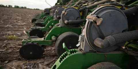 A row of green planters sits in a field, ready for planting. These machines are essential for farmers, contributing to the average hours on a tractor per year.