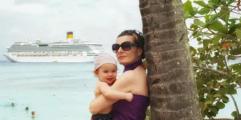 Mamma e bimbo abbracciati vicino a una palma, con una nave da crociera all'orizzonte. Una splendida posizione costa pacifica.
