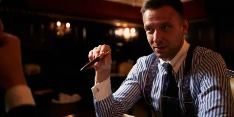 Mężczyzna w eleganckiej koszuli i krawacie trzyma pióro, zastanawiając się, ile bierze adwokat za reprezentowanie w sądzie.