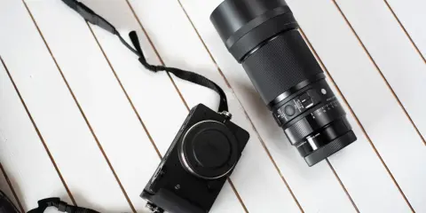 Makrofotografia sprzęt: czarny aparat Sigma fp z obiektywem 105mm f/2.8 DG DN Macro Art na białym, drewnianym tle.