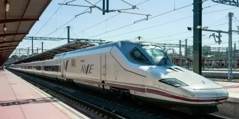 Moderner, weißer Renfe ave zug mit lila Akzenten steht auf Gleisen unter einem Bahnhofsdach.