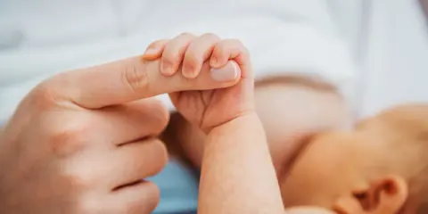 Dłoń noworodka ściska palec dorosłego. Delikatny uścisk, który budzi pytanie: czy można przekarmić noworodka?