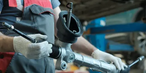 Meccanico con guanti bianchi tiene un nuovo sterzo macchina, pronto per l'installazione.