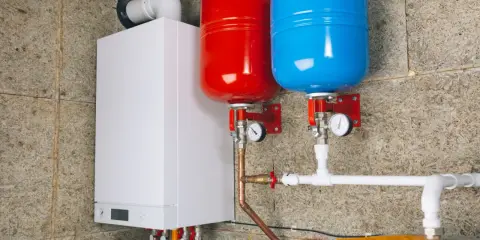 Nowoczesny kocioł z dwoma zbiornikami (czerwonym i niebieskim) i instalacją hydrauliczną. To przyszłość ogrzewania, bo zakaz pieców gazowych zbliża się wielkimi krokami.
