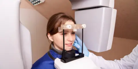 Młoda kobieta poddawana badaniu pantomograficznemu. Dowiaduje się, badanie OCT co to jest i jak pomaga w diagnostyce.