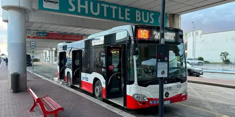 Autobus wahadłowy na przystanku lotnisko. Czerwona ławka czeka na pasażerów.