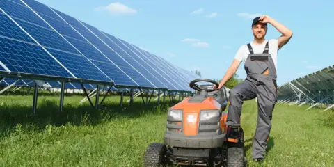 Rolnik w ogrodniczkach odpoczywa przy traktorku, obok rzędy paneli słonecznych zapewniających czystą energię dla wsi.