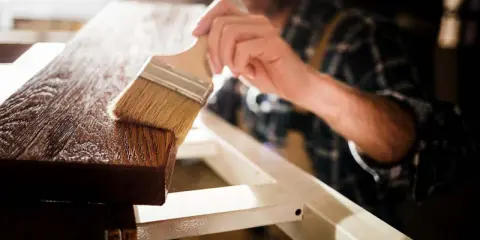 Un artesano aplica barniz a la madera con una brocha, resaltando su veta y dándole un acabado protector.