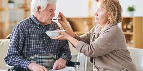 Una donna nutre con un cucchiaino il suo anziano nonno, che non mangia più, seduto su una sedia a rotelle.