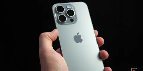 Dłoń trzyma srebrny iPhone 15 Pro z widocznym modułem aparatów i logo Apple. Dynamic Island na ekranie tego modelu to innowacja.