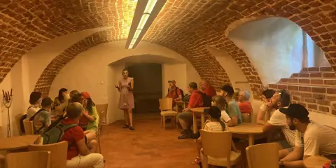 Grupa zwiedza piwnice pałacu w Poddębicach. Przewodniczka opowiada o historii miejsca.