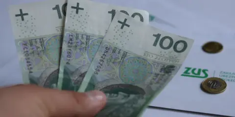 Trzy stuzłotowe banknoty w dłoni, obok dokument ZUS i monety. Czy to 30 krotność zus 2025?