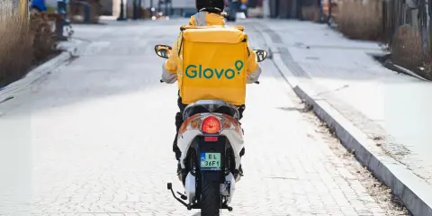 Kurier Glovo na skuterze, w żółtej kurtce z logo, przemierza ulicę. Zastanawiasz się, ile zarabia pracownik Glovo?