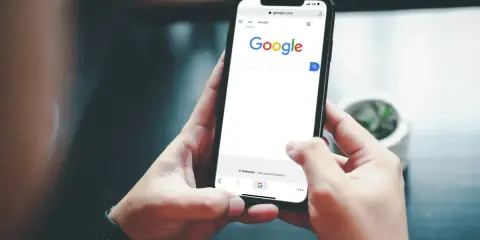 Ręce trzymające smartfon z otwartą wyszukiwarką Google. Szukasz informacji, jak usunąć konto Google z telefonu po resecie?