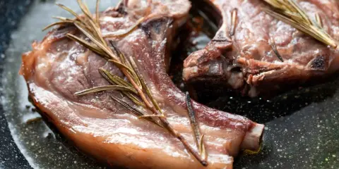 Due braciole di maiale succulente cuociono in padella con rametti di rosmarino.