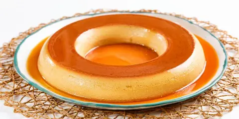 Un delicioso flan de café, con su caramelo dorado, reposa en un plato blanco con borde azul, sobre una esterilla tejida.