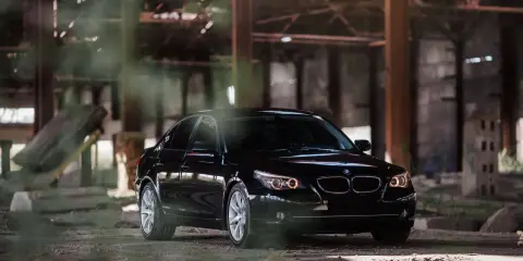 Czarny BMW 535d w opuszczonej hali, otoczony mgłą i gruzem.
