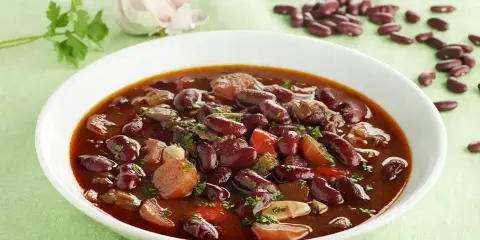 Un plato humeante de judías pintas con trozos de carne y verduras, decorado con perejil fresco.