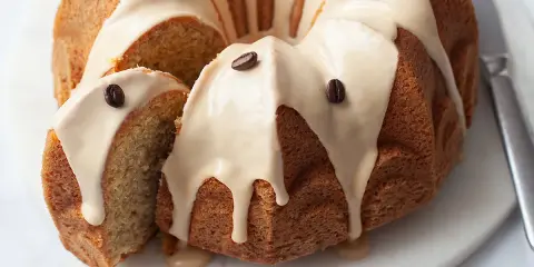 Deliziosa torta al caffè con glassa chiara e chicchi di caffè come decorazione. Una fetta è stata tagliata, mostrando la morbida consistenza interna.