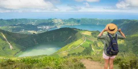 Frau mit Hut und Rucksack genießt den Ausblick auf die Azoren. Perfekte azoren beste reisezeit für dieses Panorama.