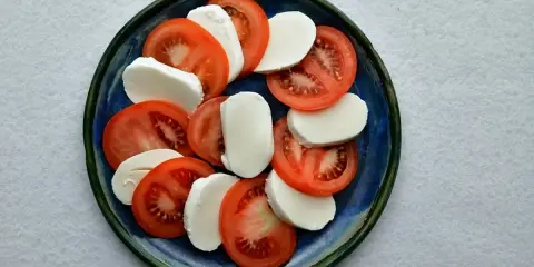 Plasterka pomidorów i mozzarelli ułożone naprzemiennie na niebieskim talerzu.