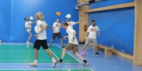 Mężczyźni w koszulkach z amerykańską flagą grają w gry zespołowe dla dorosłych, odbijając balony na hali sportowej.