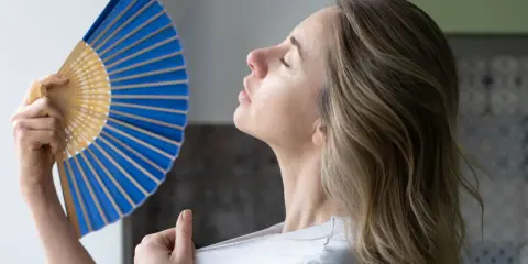 Mujer abanicándose para refrescarse, una solución para como ventilar una habitación sin ventana y combatir el calor.