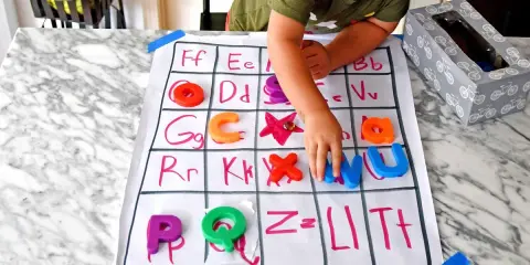 Chłopiec układa kolorowe literki na planszy z alfabetem dla dzieci. Nauka przez zabawę!