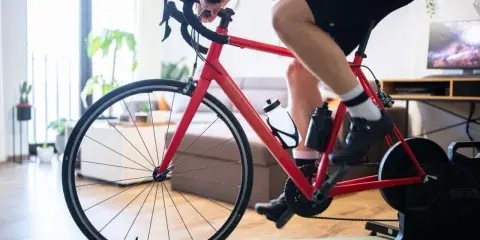 Intensywny trening na trenażerze kolarskim w domu. Czerwony rower, sportowiec w spodenkach i koszulce, butelki z wodą.