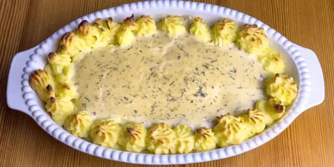 En gratinerad fiskrätt med alaska pollock recept, omgiven av spritsad potatis.