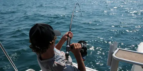 Ragazzo con cappellino nero pesca in mare, mostrando alcuni metodi di pesca con la canna.