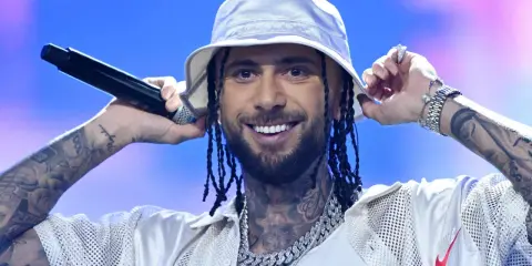 Malik Montana we Wrocławiu, w białym bucket hat, z mikrofonem w dłoni, uśmiecha się do fanów.