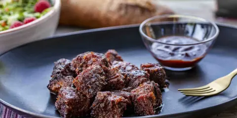 Saftige, karamellisierte **burnt ends** auf einem Teller mit BBQ-Sauce und Salat. Ein Fest für Fleischliebhaber!