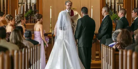 Para Młoda klęczy przed ołtarzem, składając przysięgę małżeńską w kościele katolickim. Duchowny błogosławi ich.