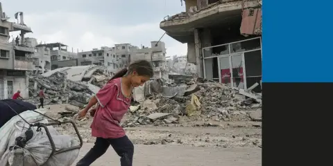 Een meisje sleept een kar met spullen door de verwoesting van de oorlog in Gaza. Gebouwen liggen in puin, een triest beeld van de impact op burgers.