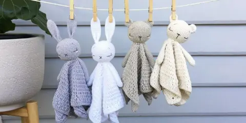 Cuatro adorables mantas de apego crochet, con forma de conejitos y ositos, cuelgan de una cuerda.