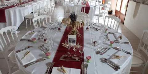 Une table dressée à la française, prête pour un événement. Nappes blanches, chemins de table bordeaux, vaisselle et couverts élégants, et une touche champêtre avec des épis de blé et de la lavande.