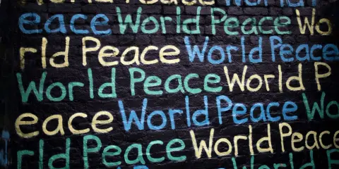 Un promemoria di Gianni Rodari: "Pace nel mondo" scritto in giallo, blu e verde su un muro di mattoni neri.