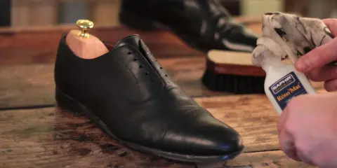 Schuhe polieren: Ein schwarzer Lederschuh mit Schuhspanner wird mit einem Tuch und Saphir Reno'Mat gereinigt.