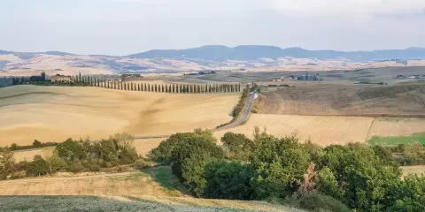 Colline dorate e cipressi iconici nel Val d'Orcia, con un borgo in lontananza. Un paesaggio da cartolina.