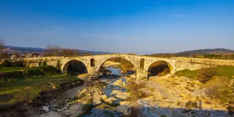 Le **pont Julien**, un ancien pont de pierre à trois arches, enjambe une rivière asséchée bordée de rochers et de végétation.